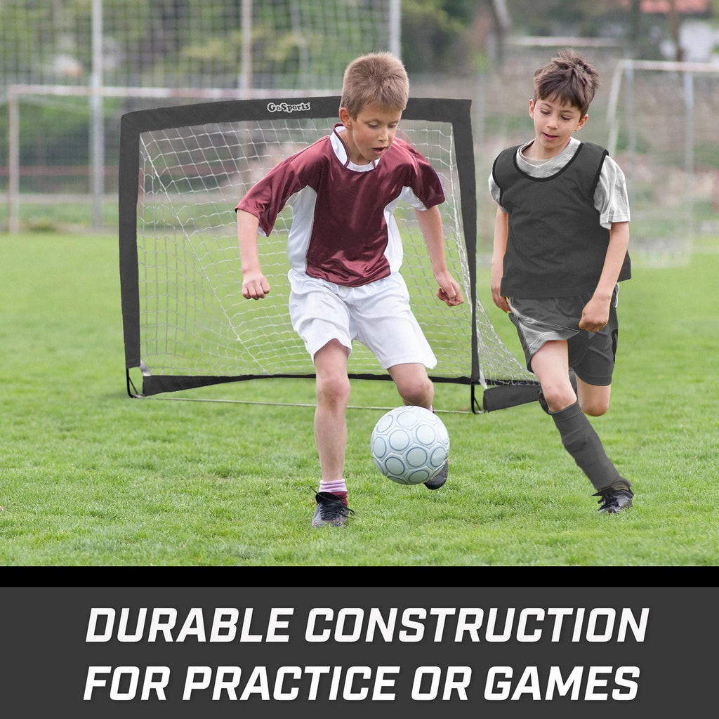 two boys playing soccer on a field with a goal