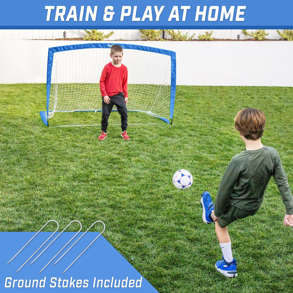 a boy kicking a soccer ball in the yard with a blue and white soccer goal