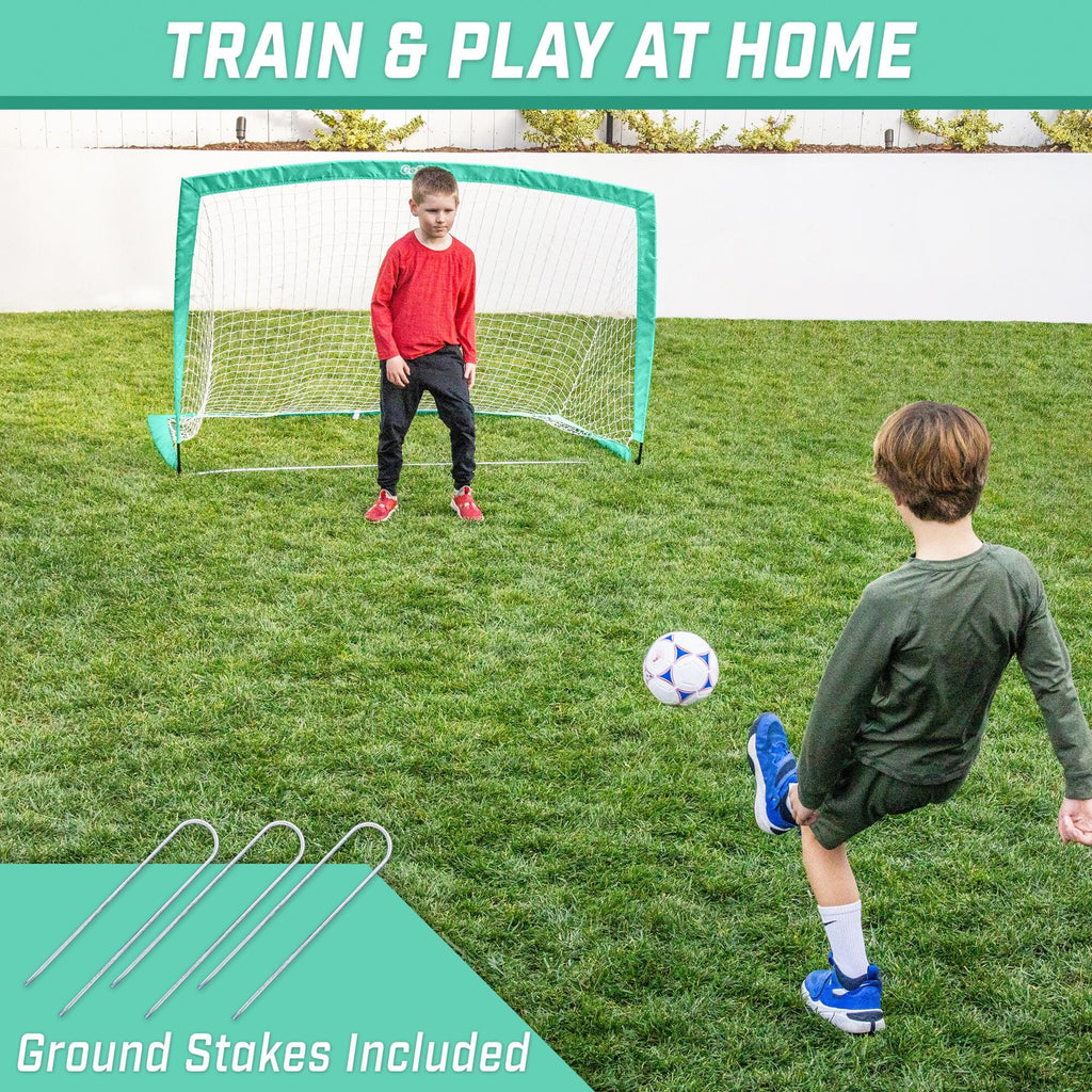 a boy kicking a soccer ball in the yard with a green and white soccer goal